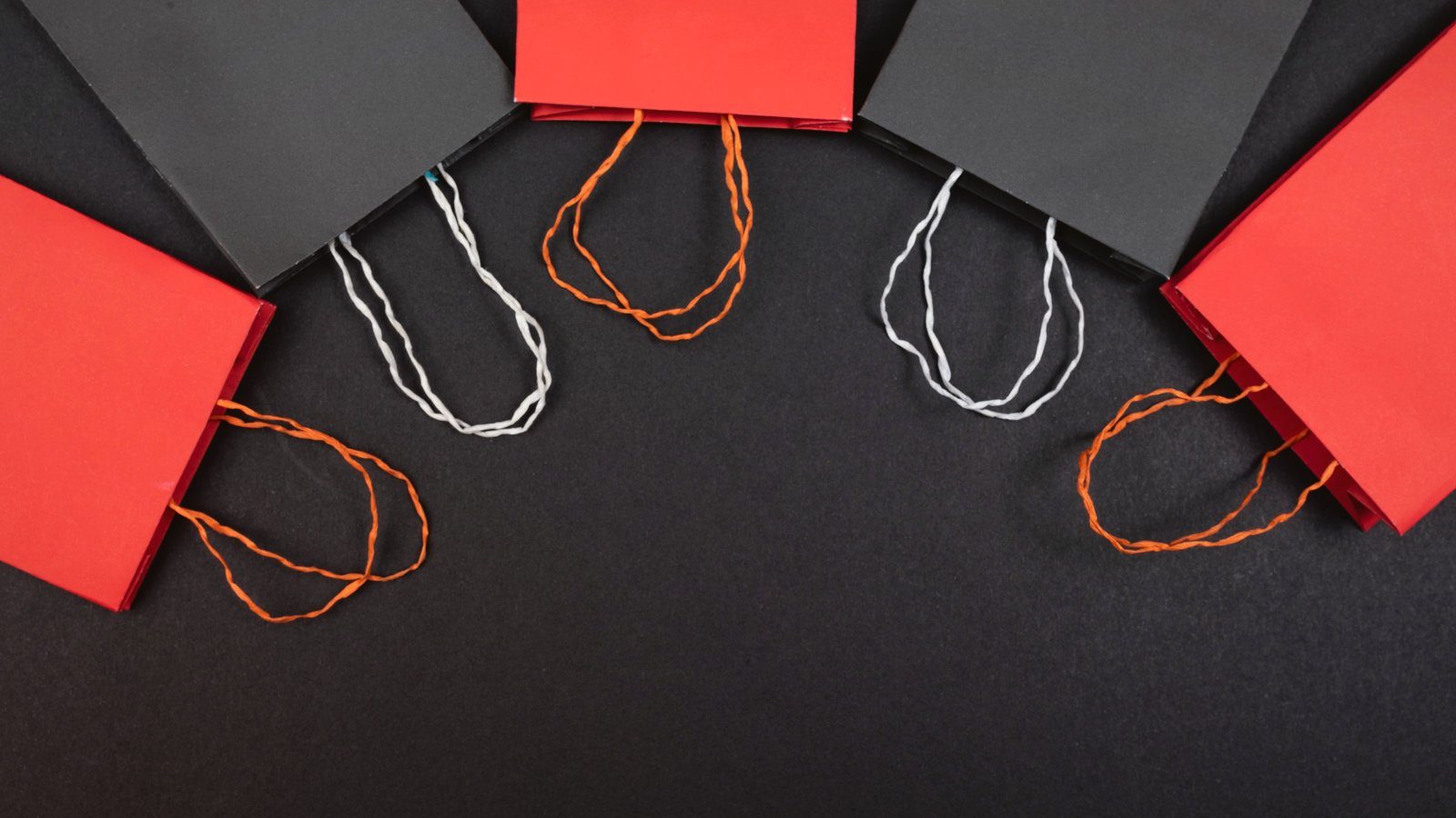 Bolsas de papel rojas y negras con asas de cordel, vistas desde arriba sobre un fondo oscuro