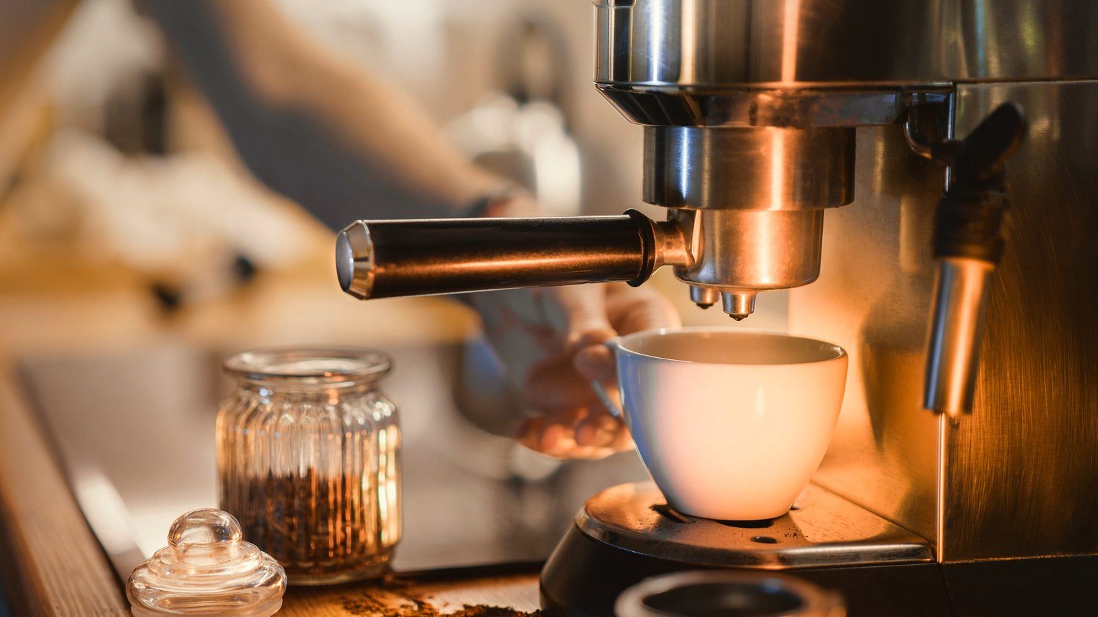 Una cafetera espresso sirviendo un café en una taza blanca, con la luz cálida de una cocina