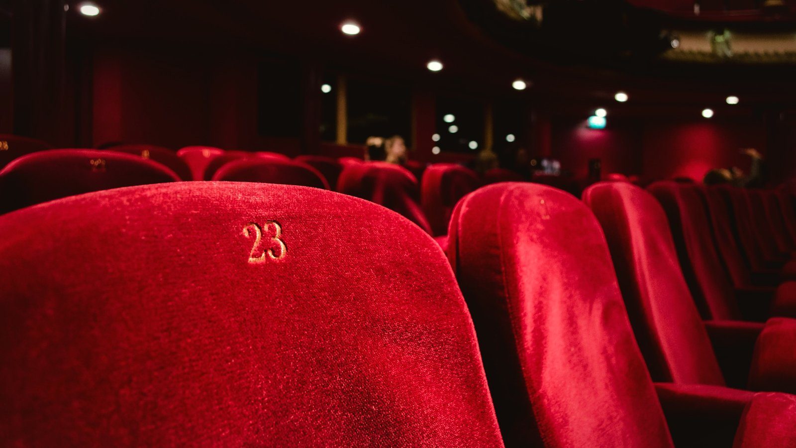 Butacas rojas de terciopelo en una sala de cine con las luces bajas; en primer plano, el respaldo de la butaca 23