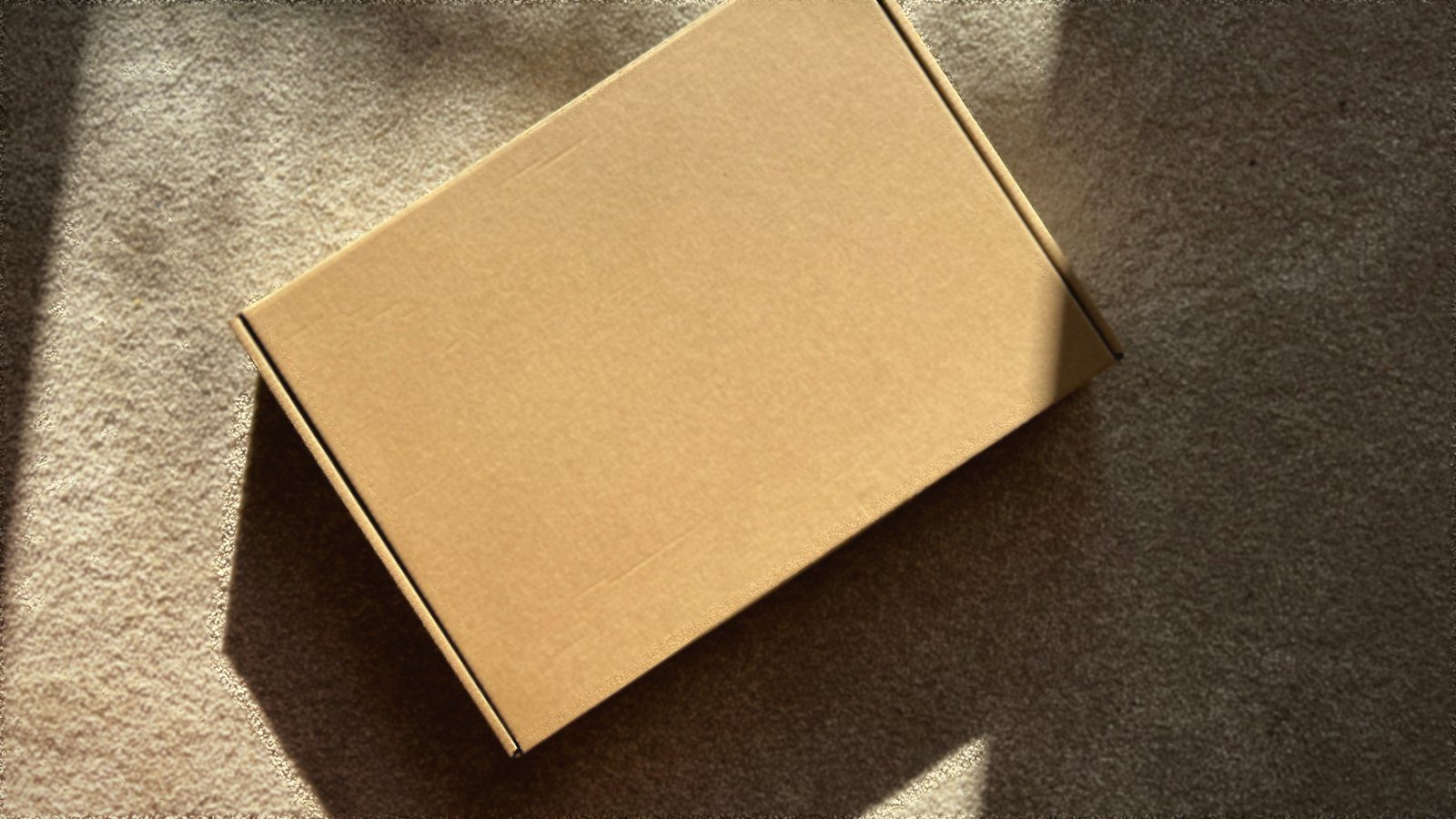 Una caja de envío de cartón sobre una superficie clara, cruzada por la luz del sol que entra por una ventana